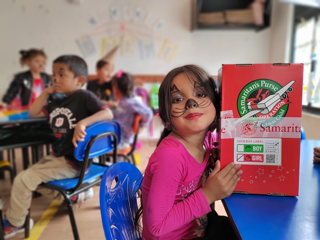 little girl with painted face costume holding Samaritans' Purse Christmas gift box