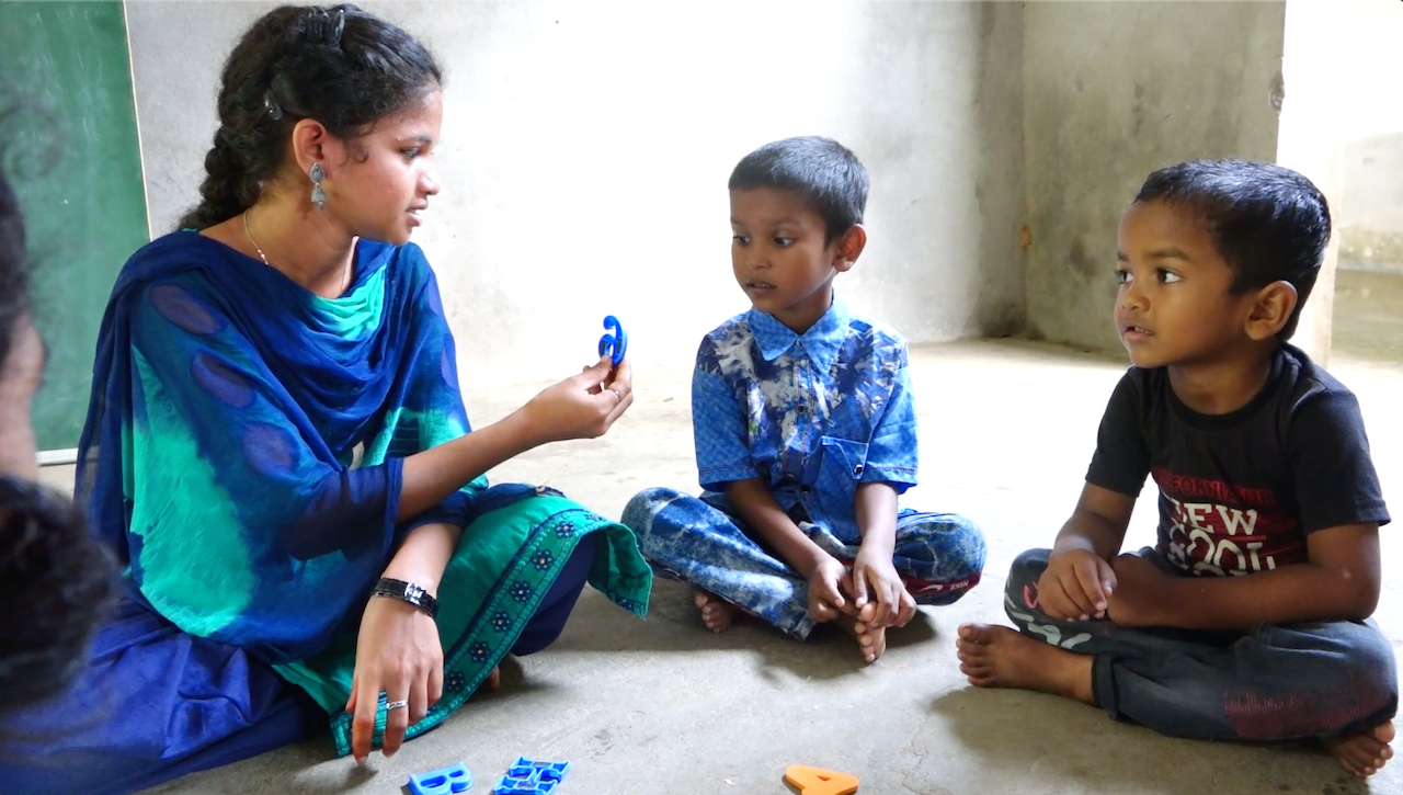 Children and teacher served by Impact Initiatives